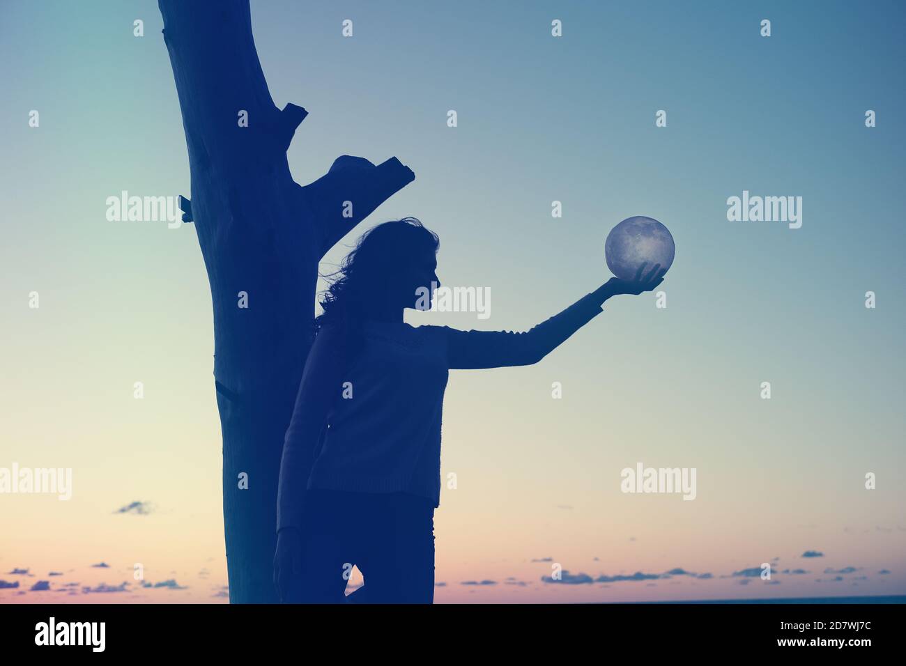 La chica sostiene la luna en sus manos. Puesta de sol en el mar. Los sueños se hacen realidad. Foto de stock