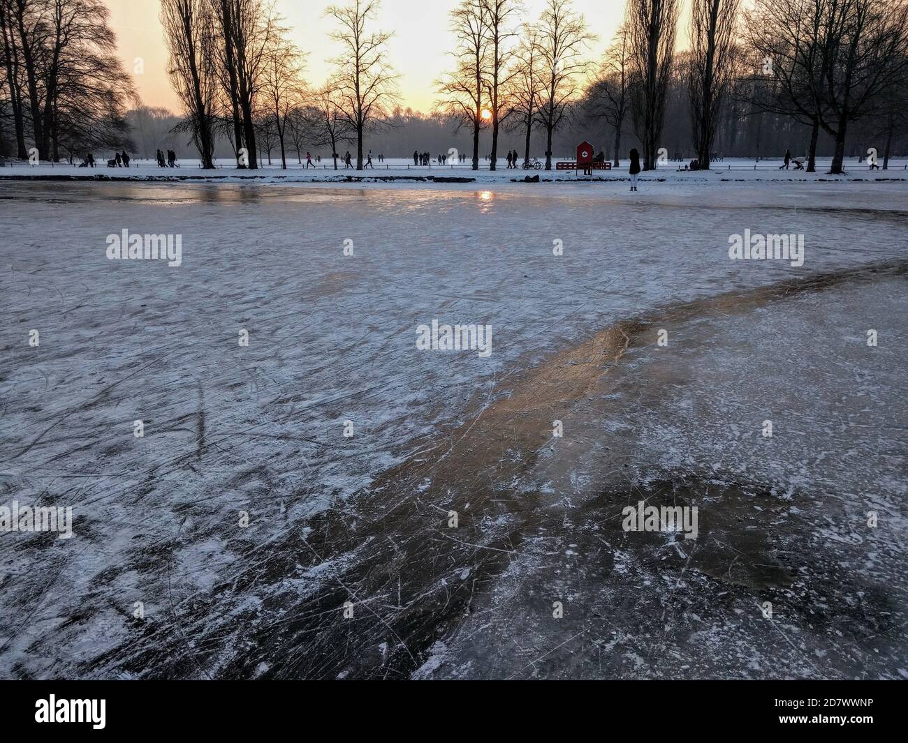 Patinaje sobre hielo en Múnich durante la puesta de sol. Lago congelado durante la puesta de sol. Patinaje sobre hielo en el lago Kleinhesseloher en Munich, Alemania. Foto de stock