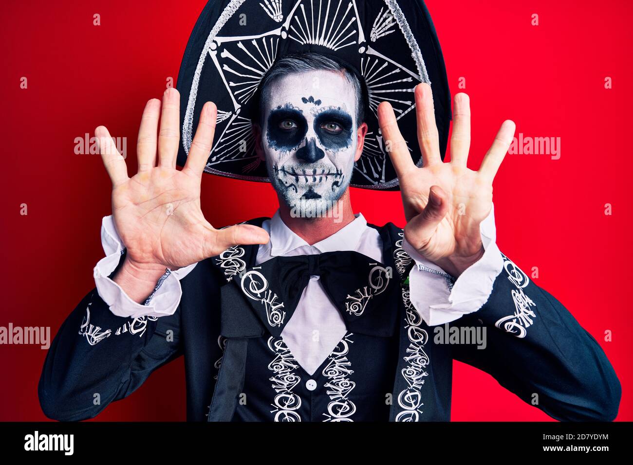 Hombre joven con traje mexicano de día muerto sobre rojo mostrando y señalando con los dedos número nueve mientras sonriendo confidente y feliz. Foto de stock