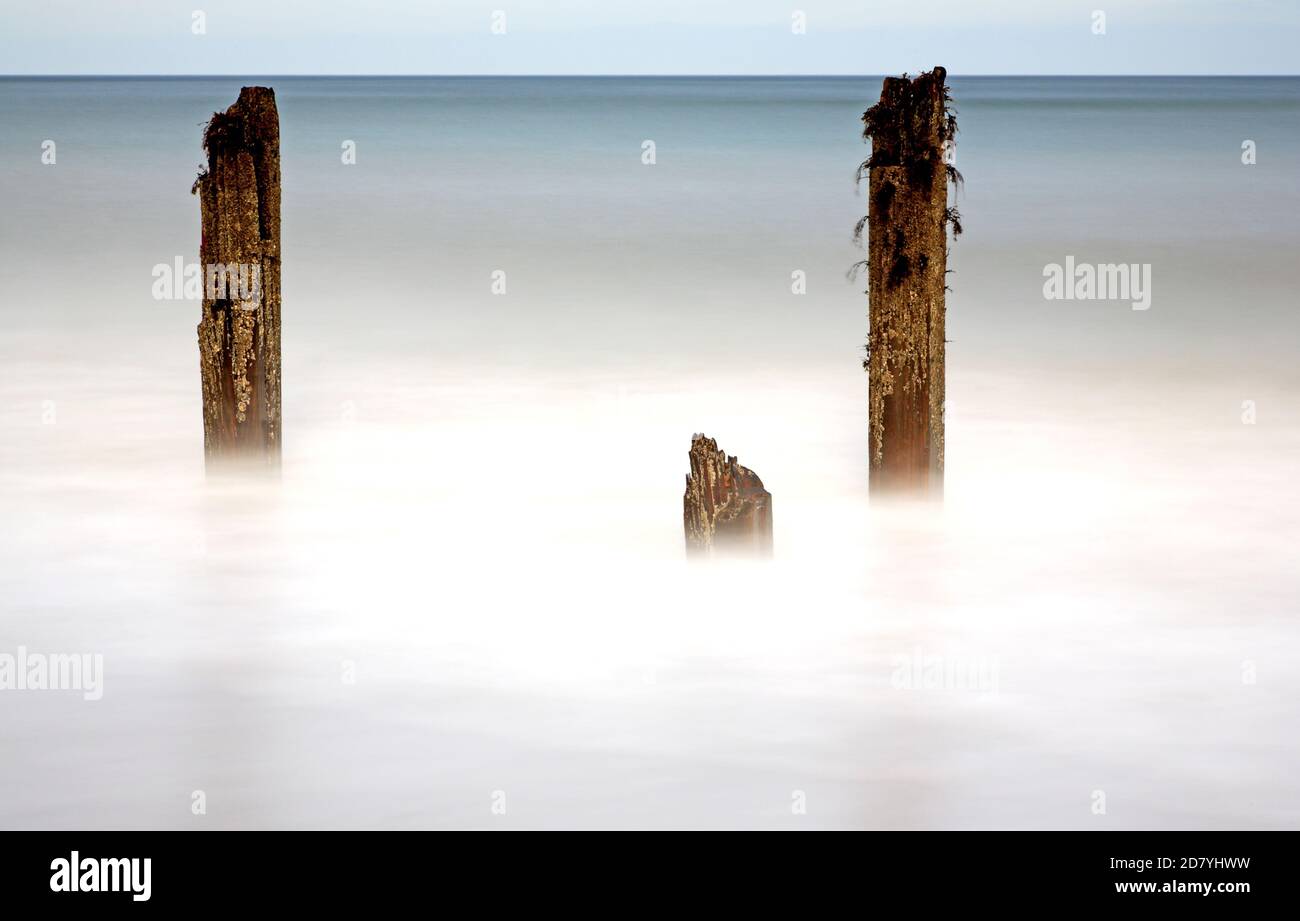 Una imagen creativa artística de tres antiguos puestos de rompeolas en el borde del mar en North Norfolk en Happisburgh, Norfolk, Inglaterra, Reino Unido. Foto de stock