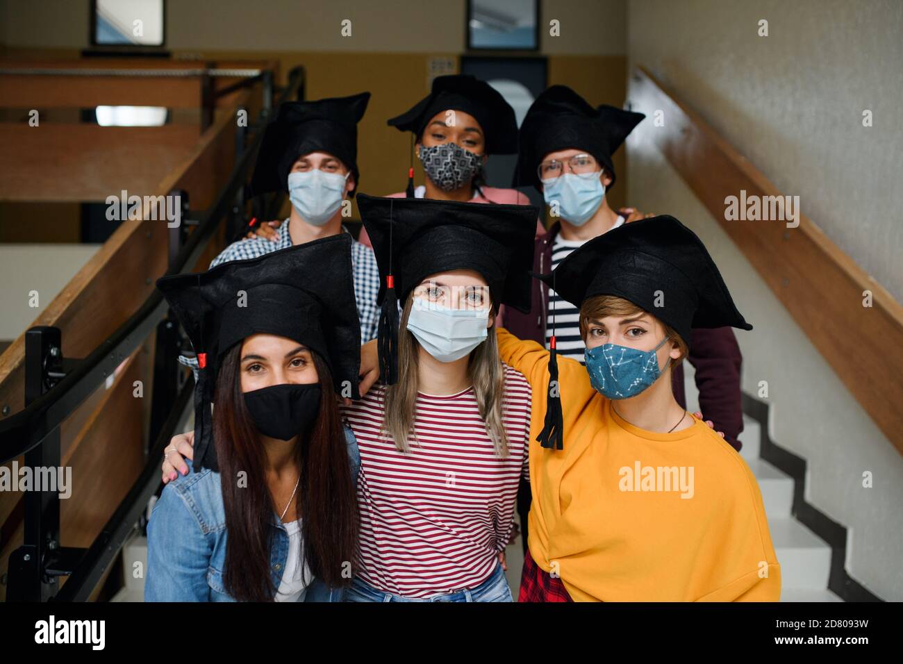 Estudiantes jóvenes con máscaras faciales y tapas de graduación en la universidad o la universidad, concepto de coronavirus. Foto de stock