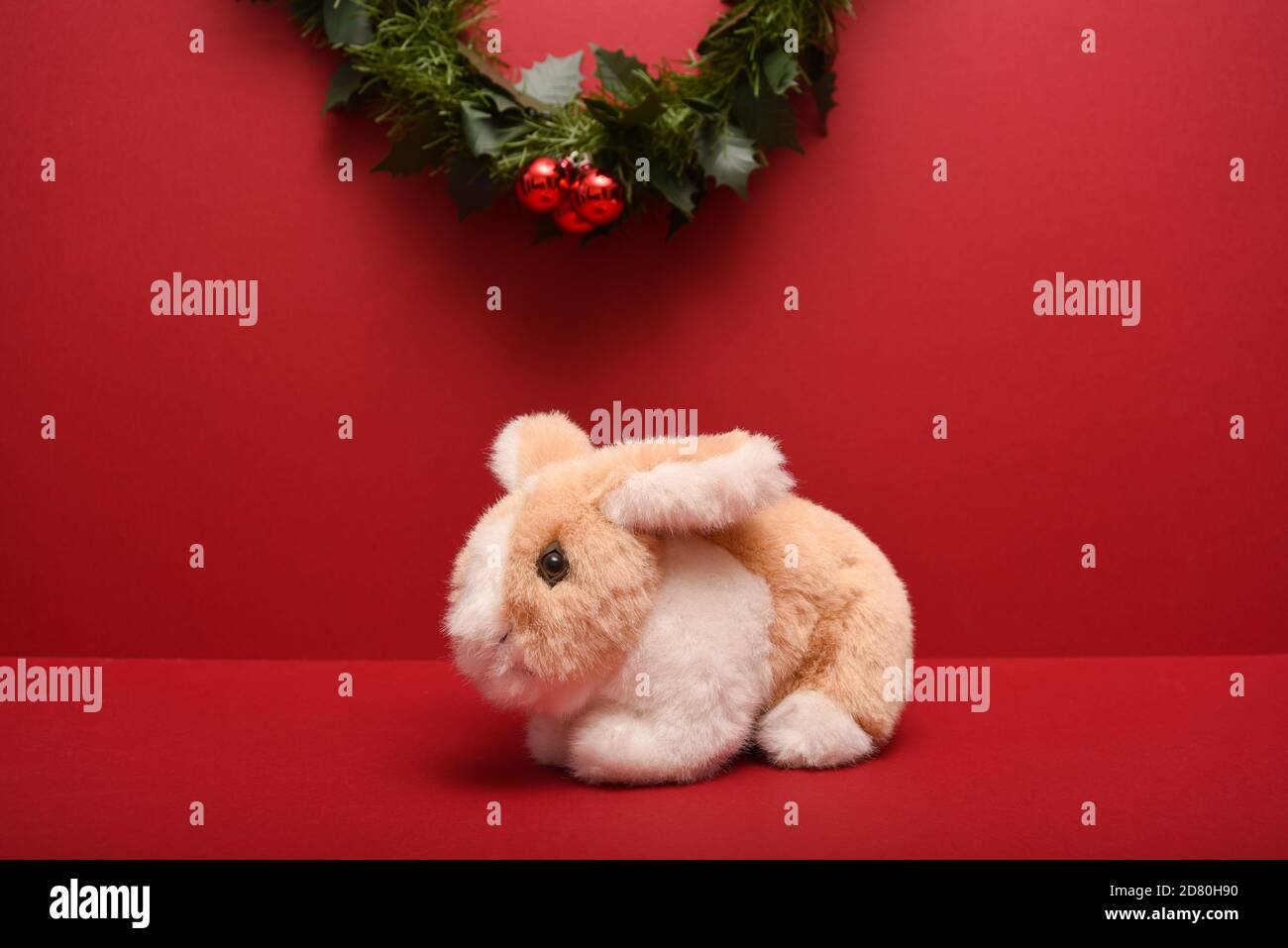 pequeño conejo de juguete relleno aislado sobre un fondo rojo debajo Una guirnalda de Navidad Foto de stock