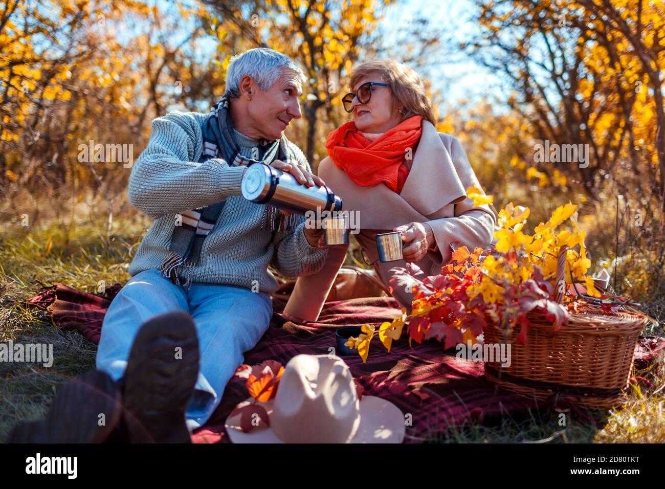 Pareja de la familia mayor que tiene té vertiendo de thermos en el bosque de otoño. Feliz hombre y mujer disfrutando de un picnic al aire libre. Foto de stock