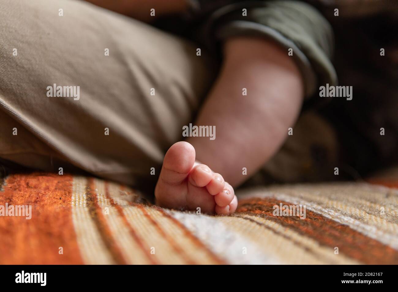 Enfoque selectivo de pequeños pies y dedos pequeños del recién nacido bebé niño que se relaja en el regazo de los padres mientras se sienta sofá en casa Foto de stock