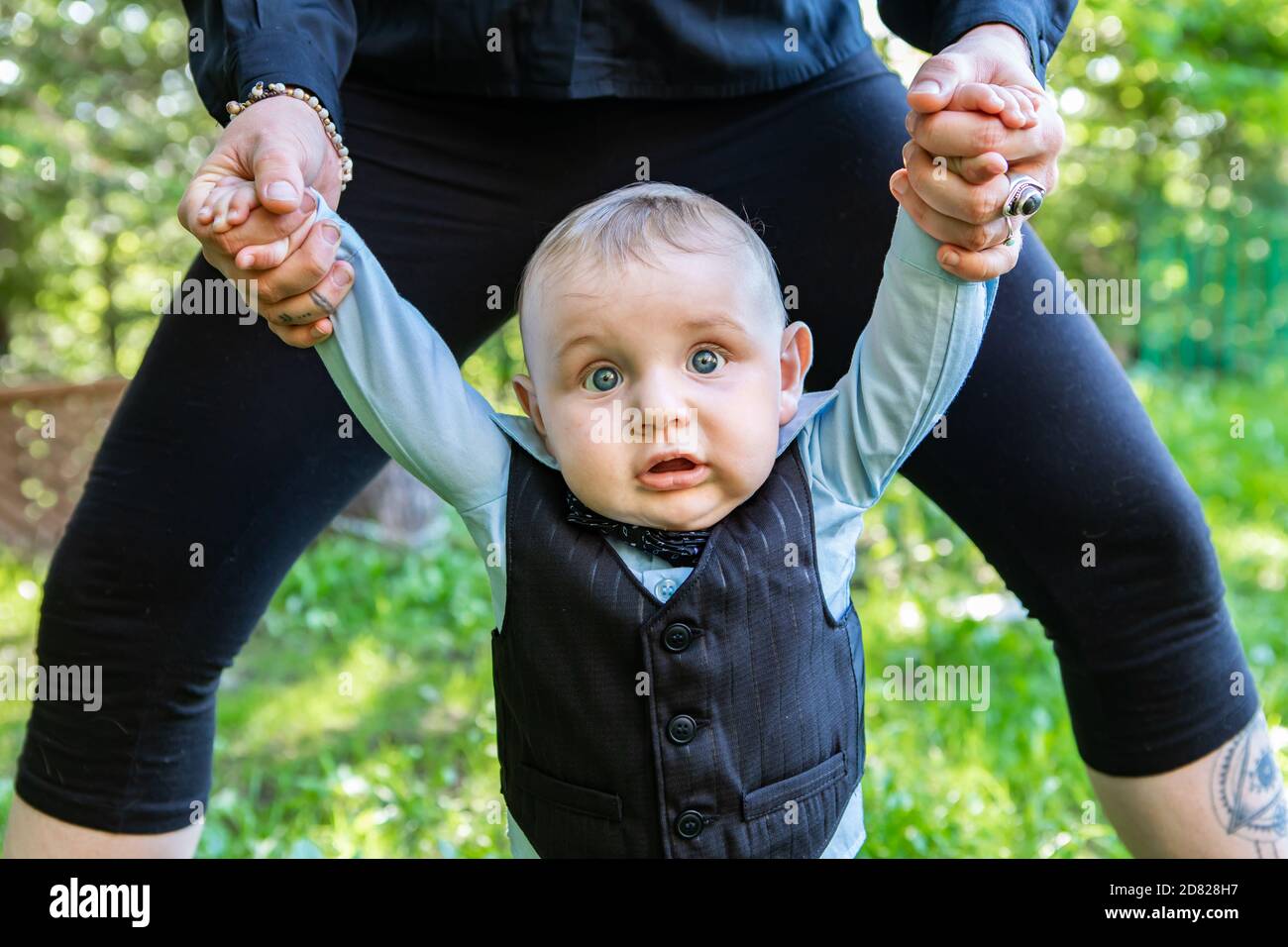 Retrato del bebé recién nacido de pie con el apoyo para las manos de los padres ropa formal posando para fotofoot en el jardín al aire libre Foto de stock