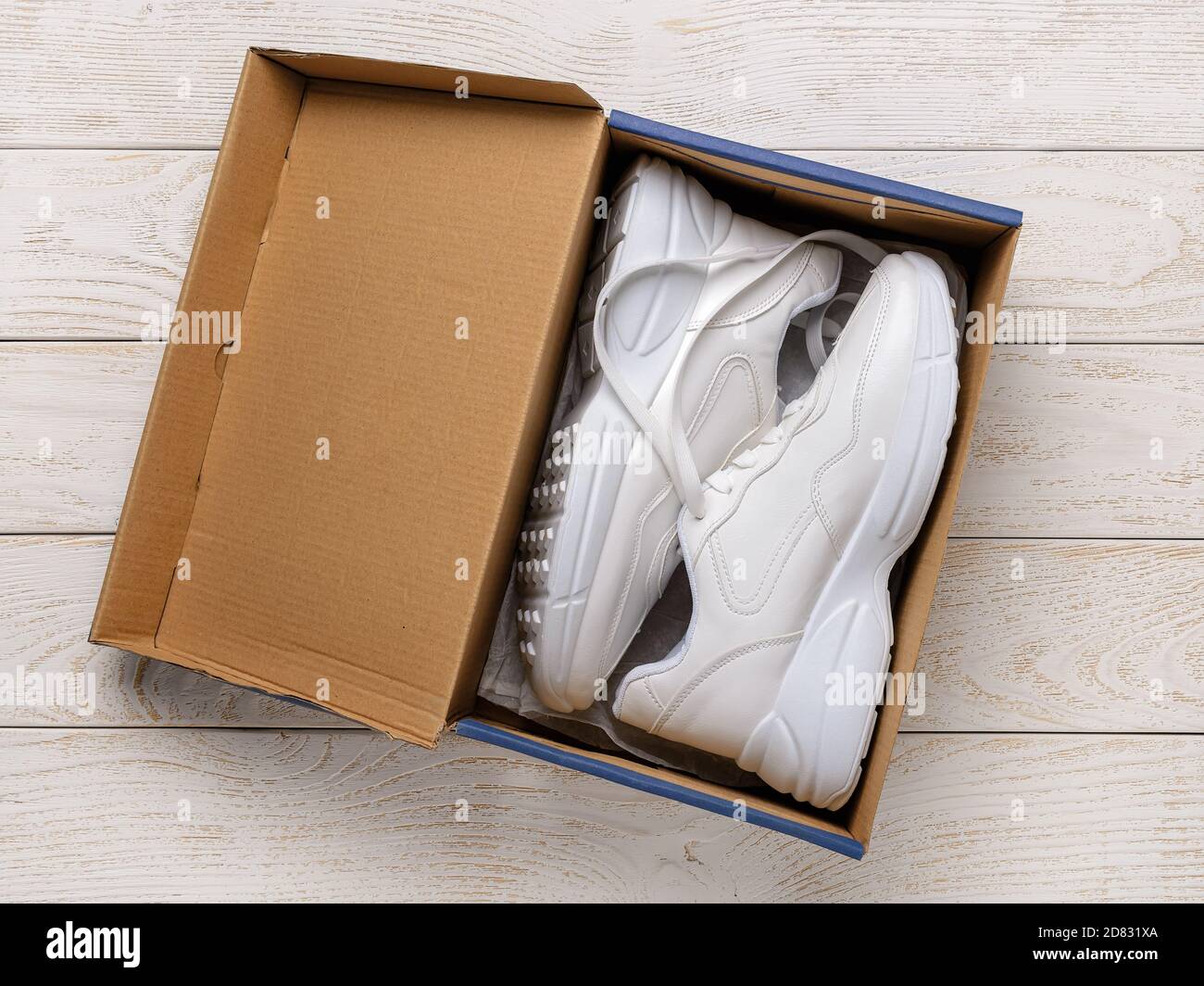 Dos sneakers de suela gruesa blanca en una caja de cartón marrón en el  suelo de madera blanca. Caja abierta con zapatos nuevos y cómodos para un  estilo de vida activo, fitness