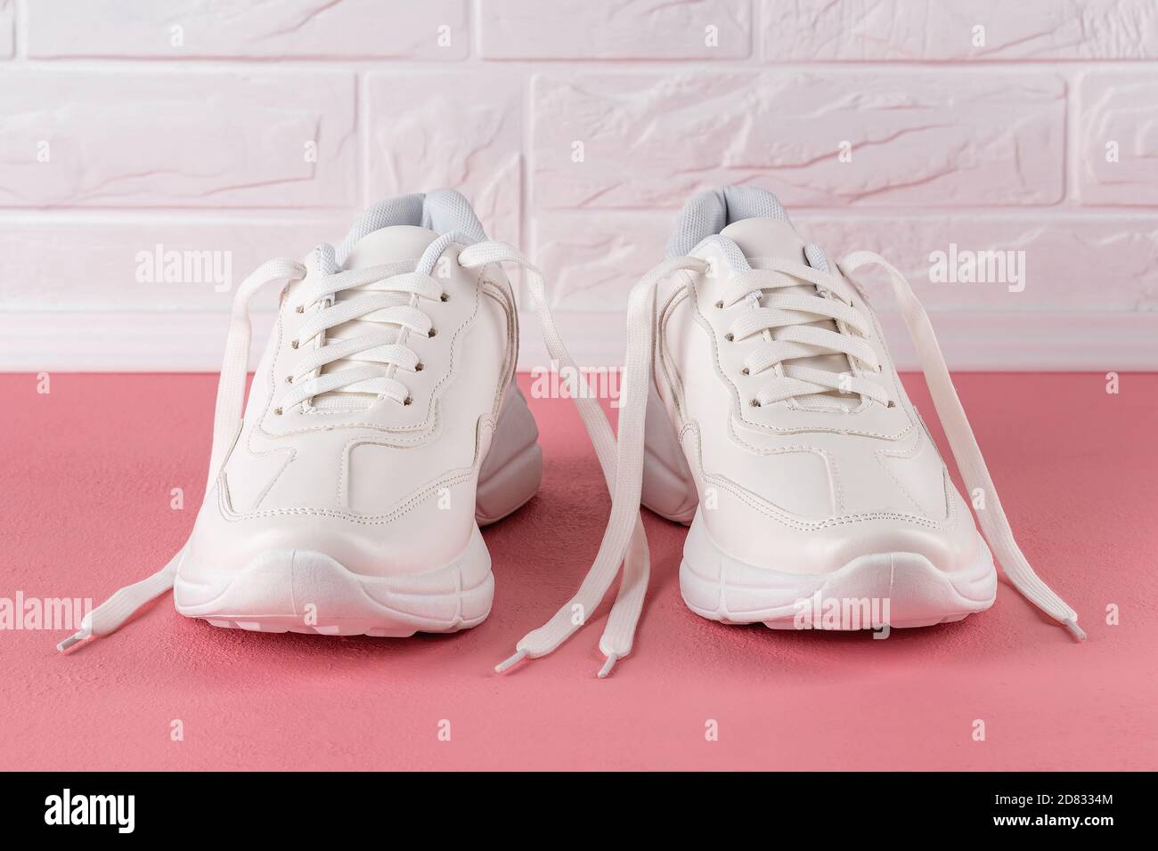 Dos sneakers blancas con suela gruesa sobre un suelo de color coral rosa.  Zapatos de cordones nuevos para mujer o adolescente para un estilo de vida  activo, fitness y deportes Fotografía de