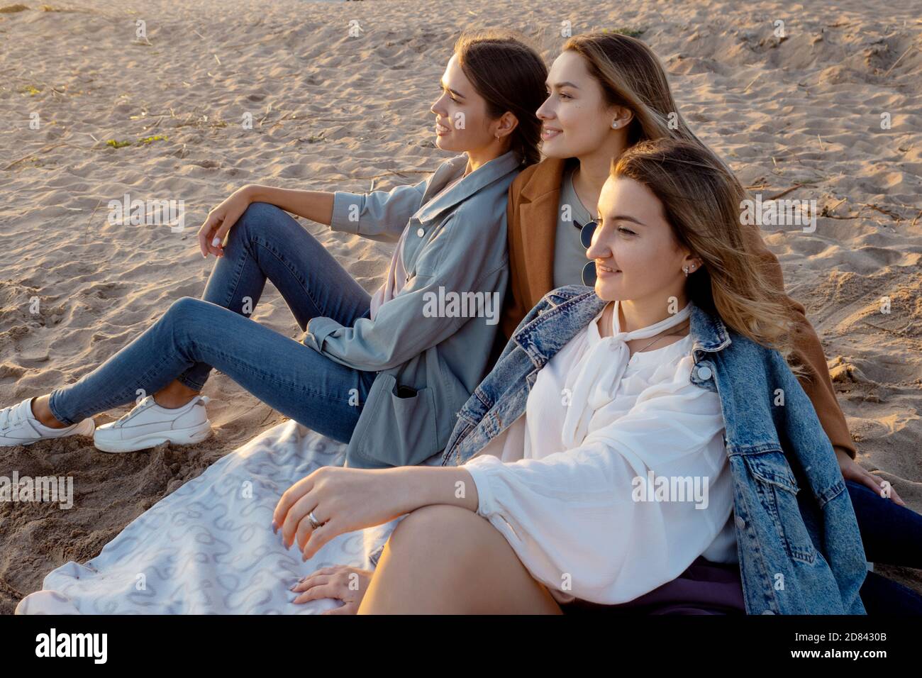 Grupo de mujeres jóvenes con ropa informal en la playa, disfrutando de la  puesta de sol. Una fiesta o una reunión de amigos, amigos se sientan en una  manta y Que se