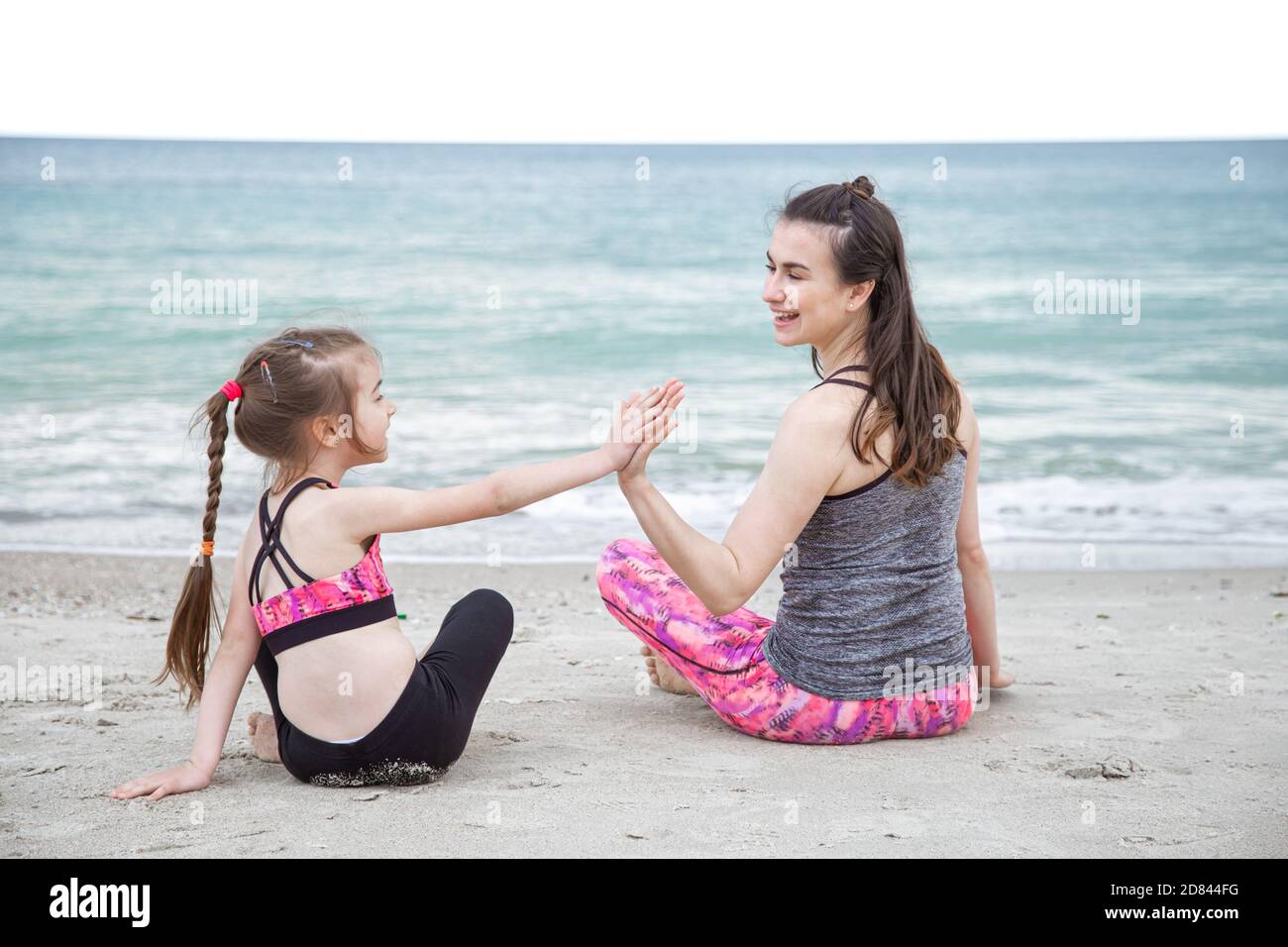 Una joven madre e hija con ropa deportiva, jugando deportes en la playa  junto al mar. Valores familiares y un estilo de vida saludable Fotografía  de stock - Alamy