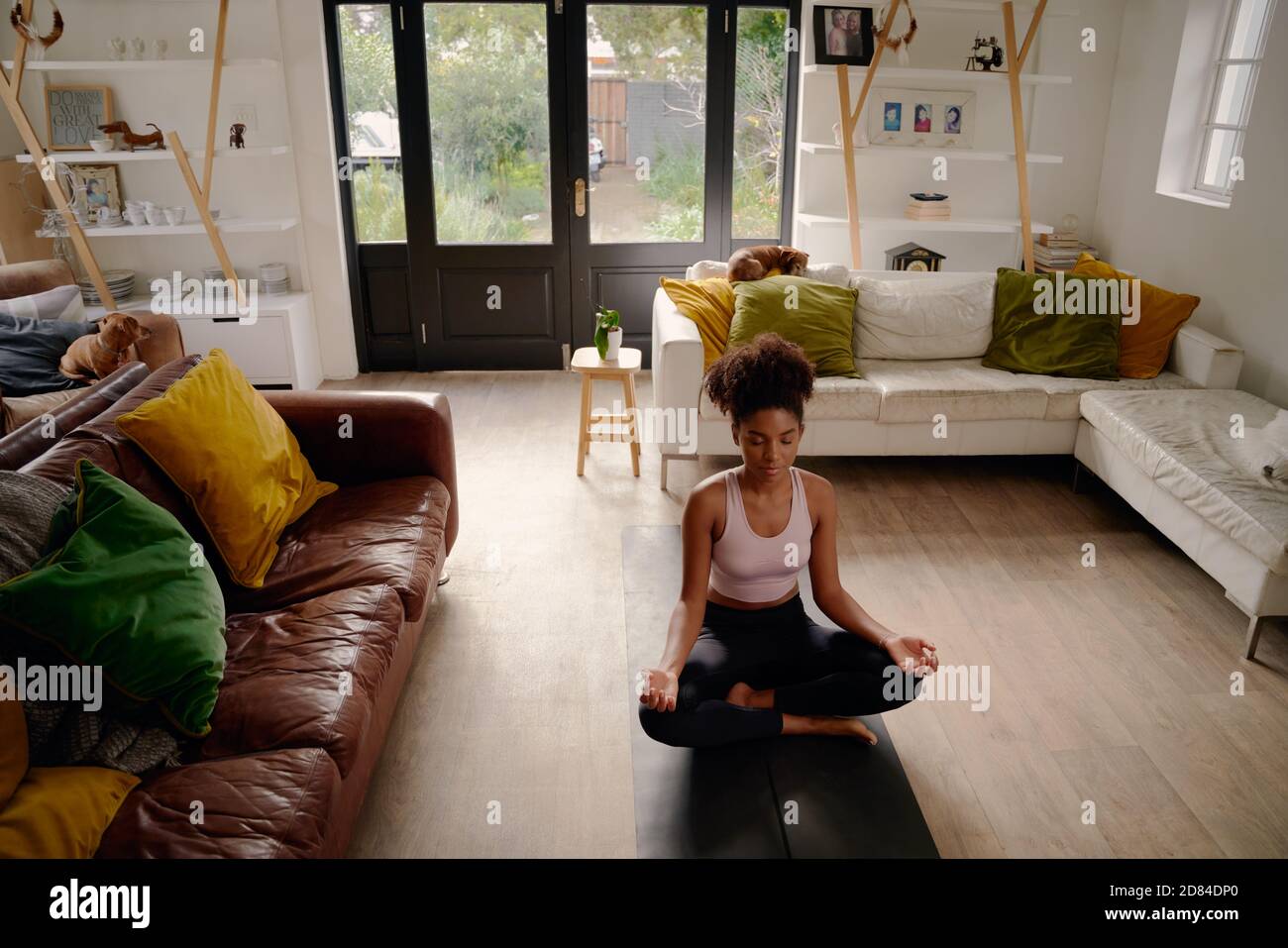 Joven mujer africana joven en posición de loto practicando la meditación y. ejercicio de respiración en la sala de estar en casa Foto de stock