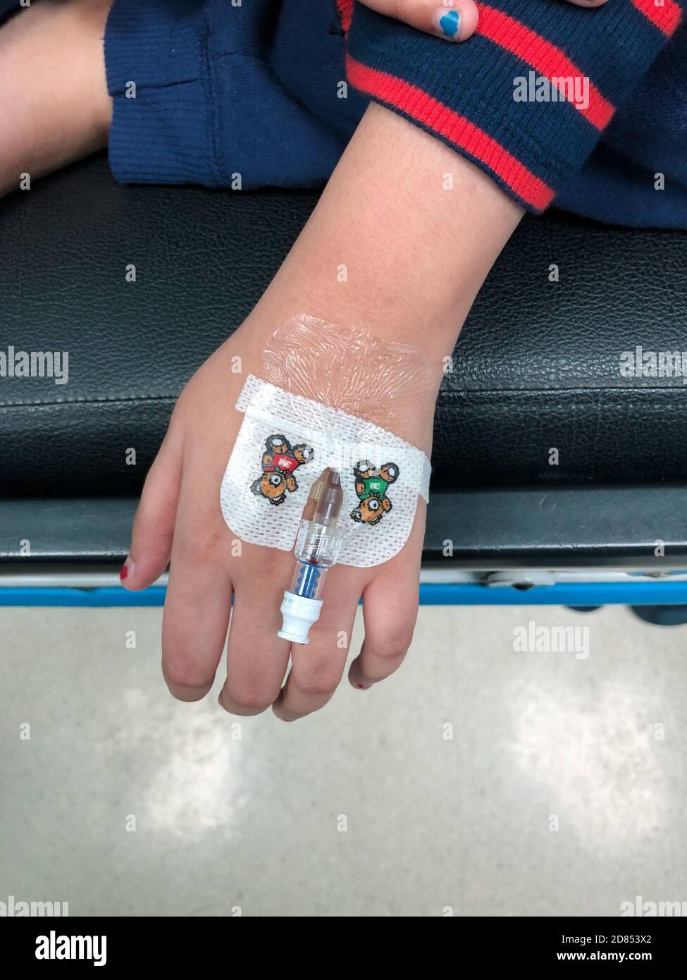 Una joven asiática con una cánula insertada en su mano izquierda en un hospital, para administrar líquidos intravenosos. Foto de stock