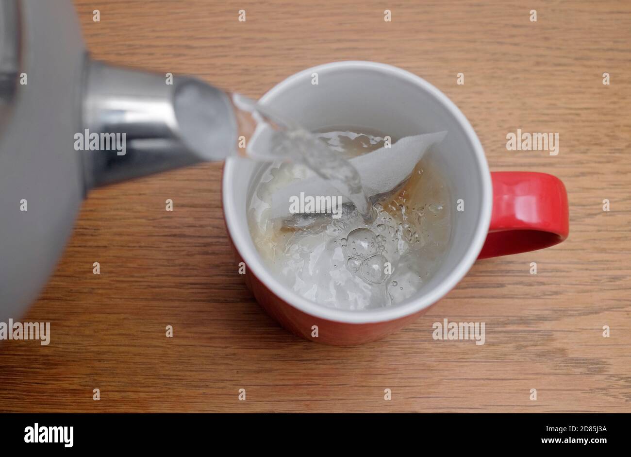 preparar una taza de té, vertiendo agua caliente sobre el tebag en una taza roja, norfolk, inglaterra Foto de stock