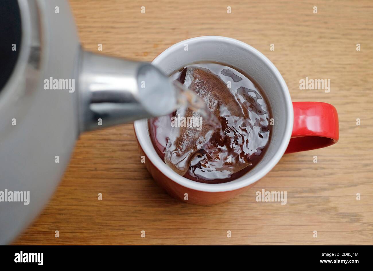 preparar una taza de té, vertiendo agua caliente sobre el tebag en una taza roja, norfolk, inglaterra Foto de stock