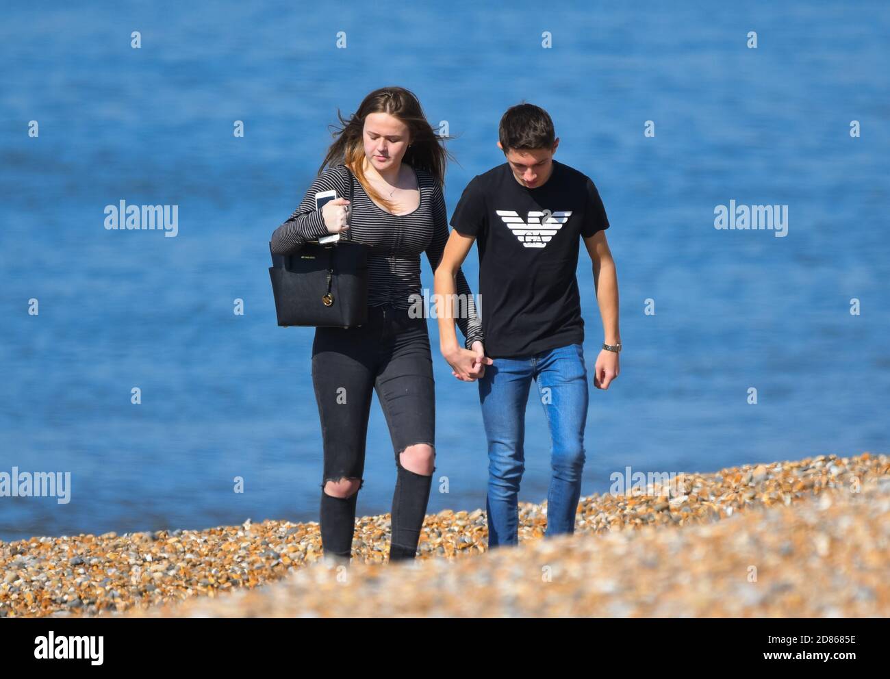 Pareja joven con las manos caminando en una playa en la costa, con el mar (océano) detrás de ellos en Inglaterra, Reino Unido. Foto de stock