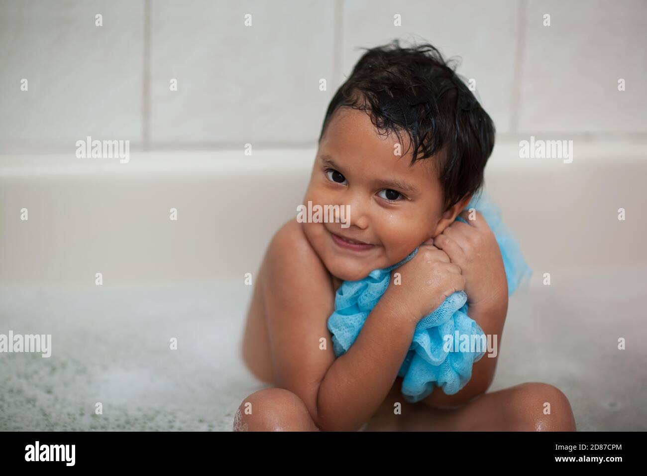 Un niño pequeño muestra que le encanta el tiempo de baño abrazando su malla de tela de lavado mientras remoja su cuerpo. Foto de stock