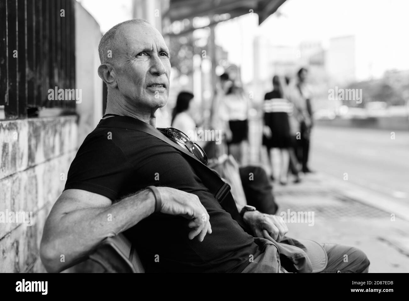 Turismo Senior calva hombre esperando y sentados en banco de madera en la parada del autobús, en Bangkok, Tailandia Foto de stock
