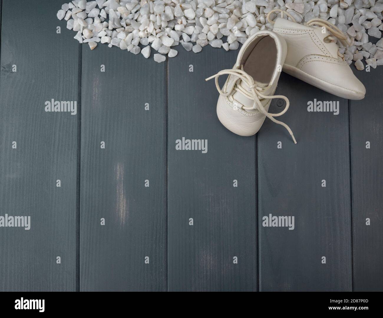 Zapatos blancos recién nacidos, con cordones atados, sobre una cama de piedras blancas y madera gris Foto de stock