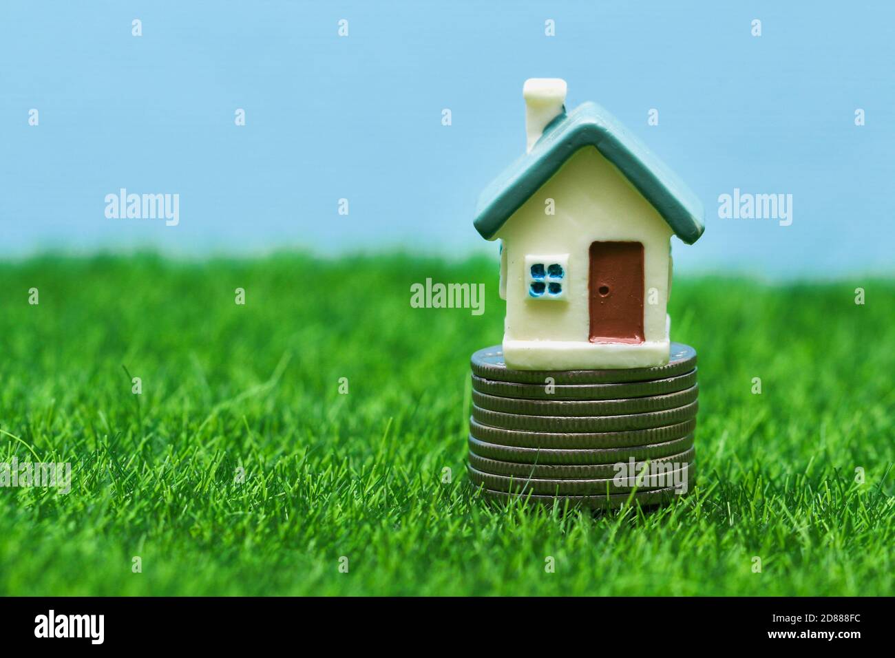 Una pequeña casa de juguete en una pila de monedas contra un fondo de hierba y cielo. Concepto de vivienda, hipoteca, préstamo. Foto de stock