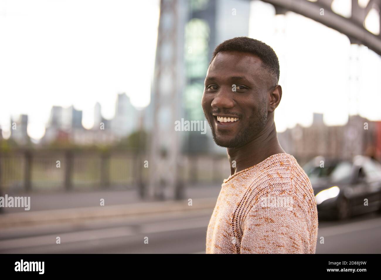 Hombre negro guapo sonriendo para cámara posando en la calle. Disparo medio. Profundidad de campo reducida. Foto de stock