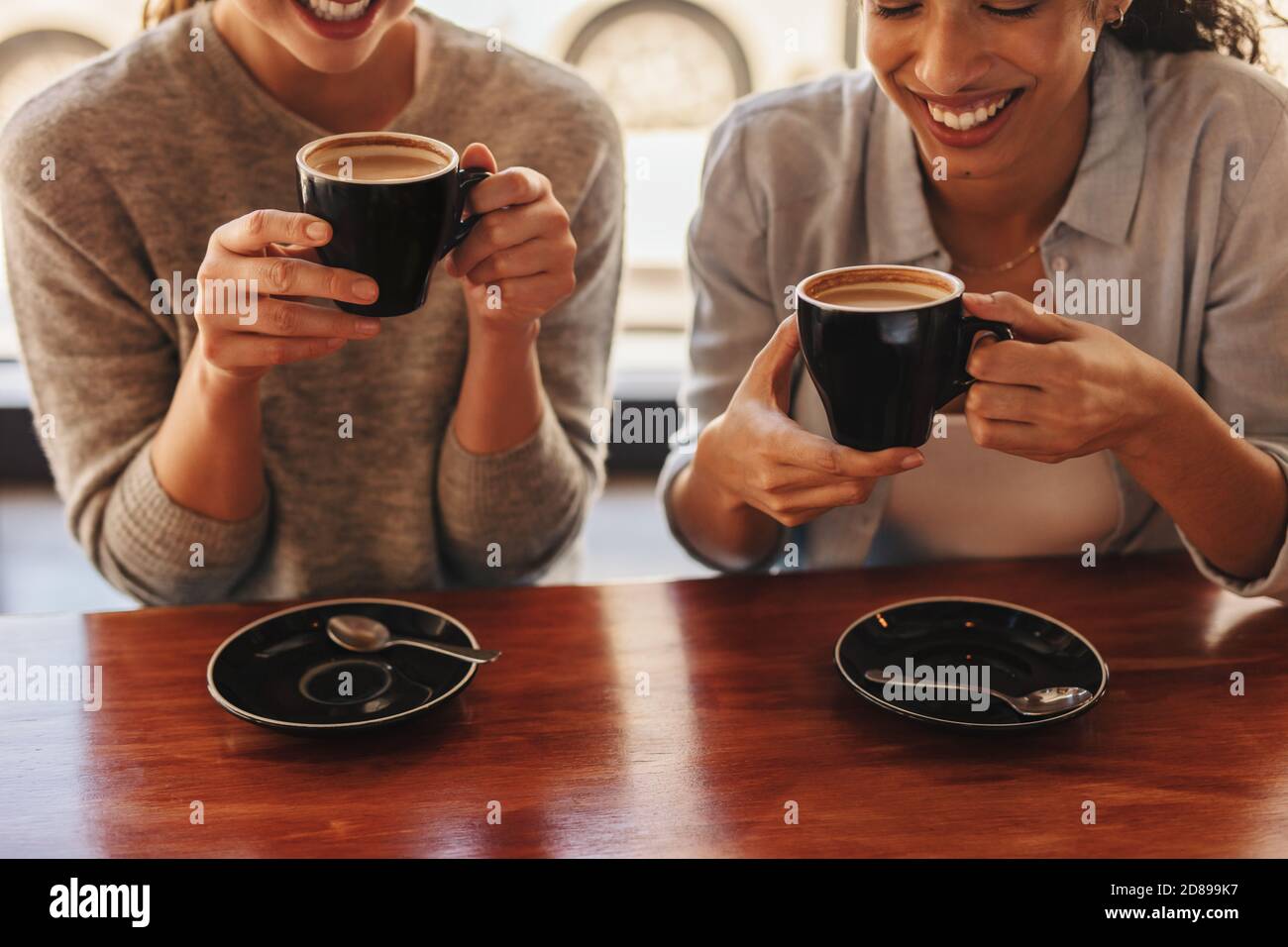 Primer plano de dos mujeres sentadas en la mesa del café bebiendo café. Amigas tomando café en una cafetería. Foto de stock