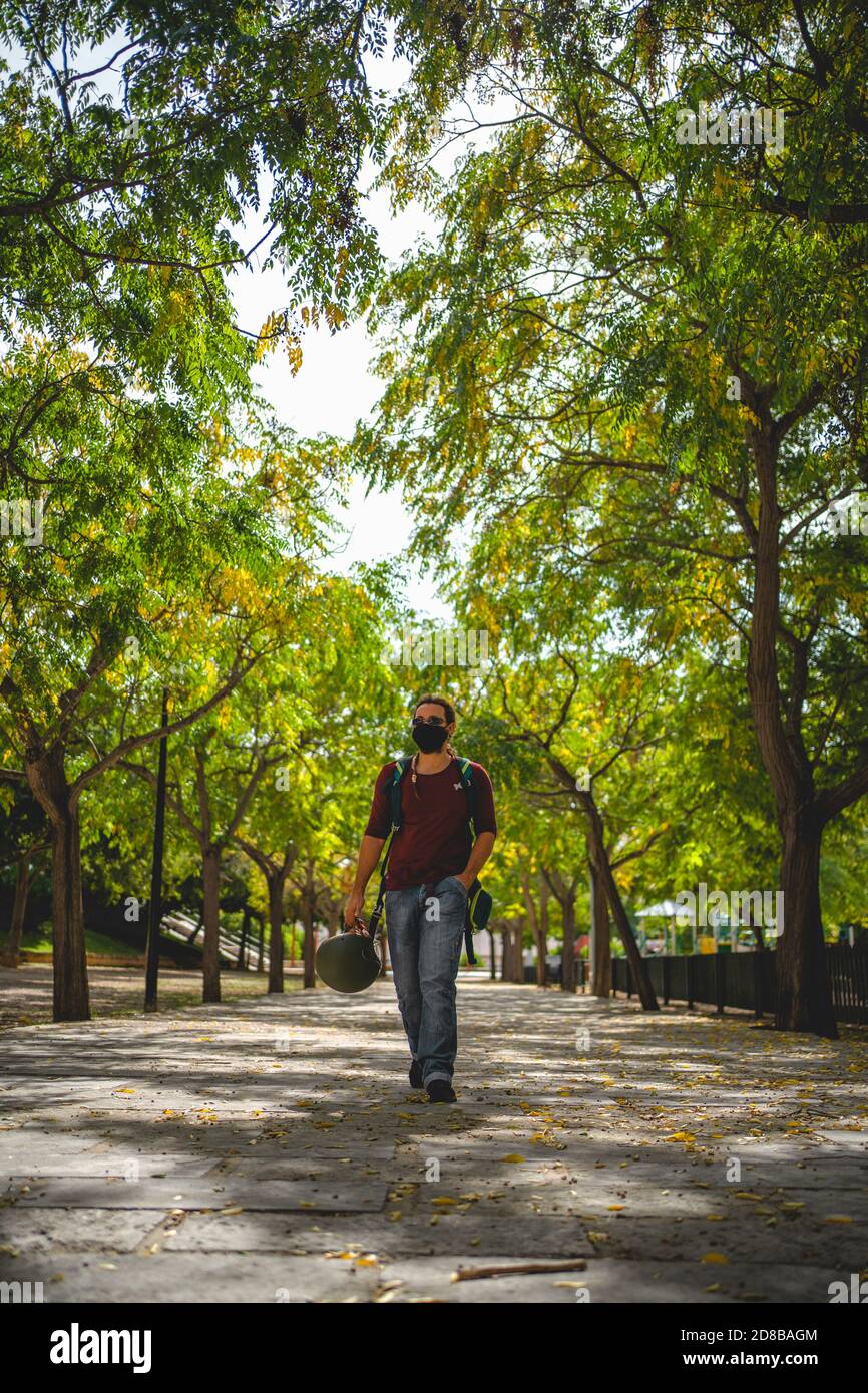El hombre camina a través de un parque sosteniendo un casco de moto durante otoño Foto de stock