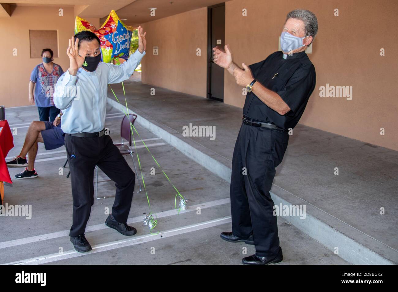 Un sacerdote asiático americano que sale hace una danza celebratoria mientras su monseñor se aferna en una iglesia católica del sur de California. Observe las mascarillas debido a la cor Foto de stock