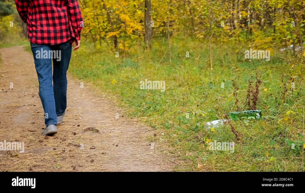 Un hombre irreconocible lanza una botella de plástico en la hierba del bosque. Foto de stock