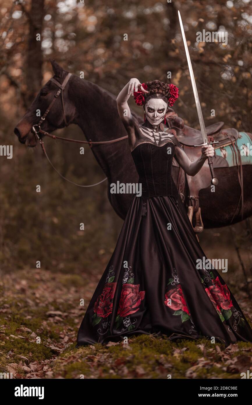 Mujer joven vestida como el símbolo mexicano del día de la calavera muerta  en un vestido negro posando adentro el bosque con un caballo Fotografía de  stock - Alamy