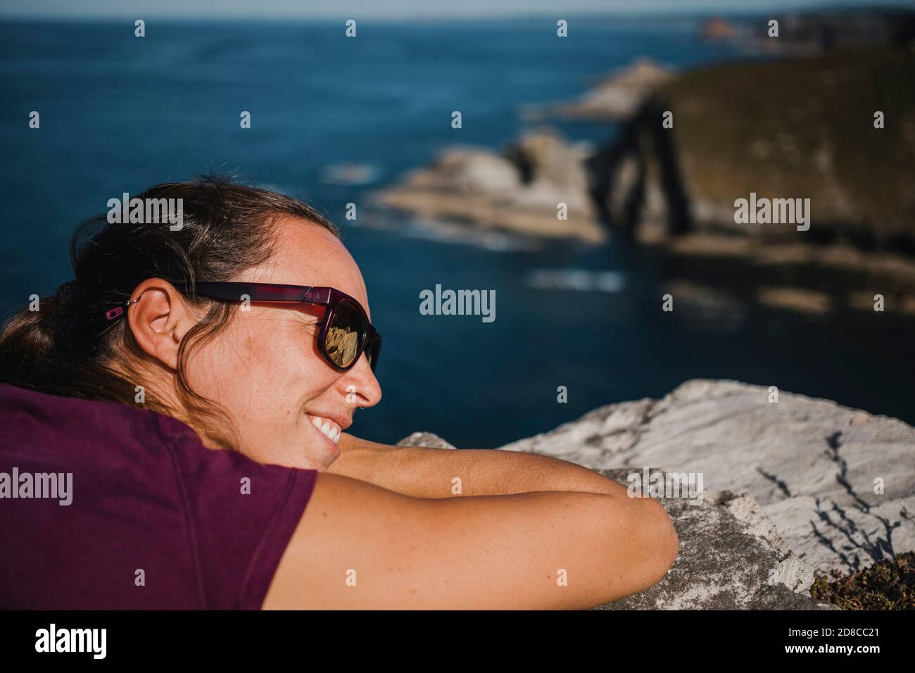 Mujer acostada en una roca, en la costa con gafas de sol y camiseta  púrpura, y el mar en el fondo Fotografía de stock - Alamy