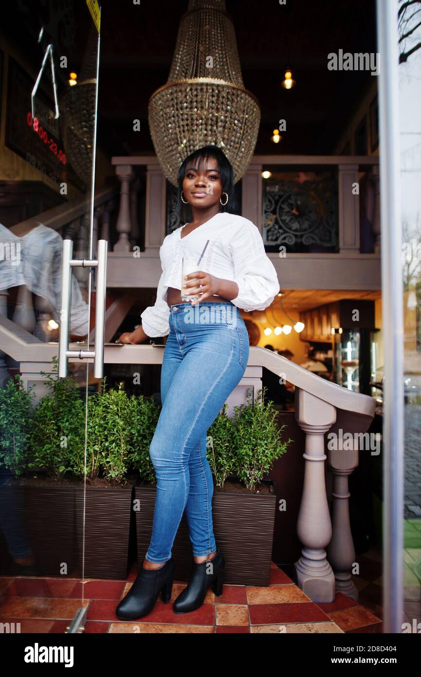 Mujeres afroamericanas con estilo en blusa blanca y jeans azules posados en  un café con latte de caramelo Fotografía de stock - Alamy