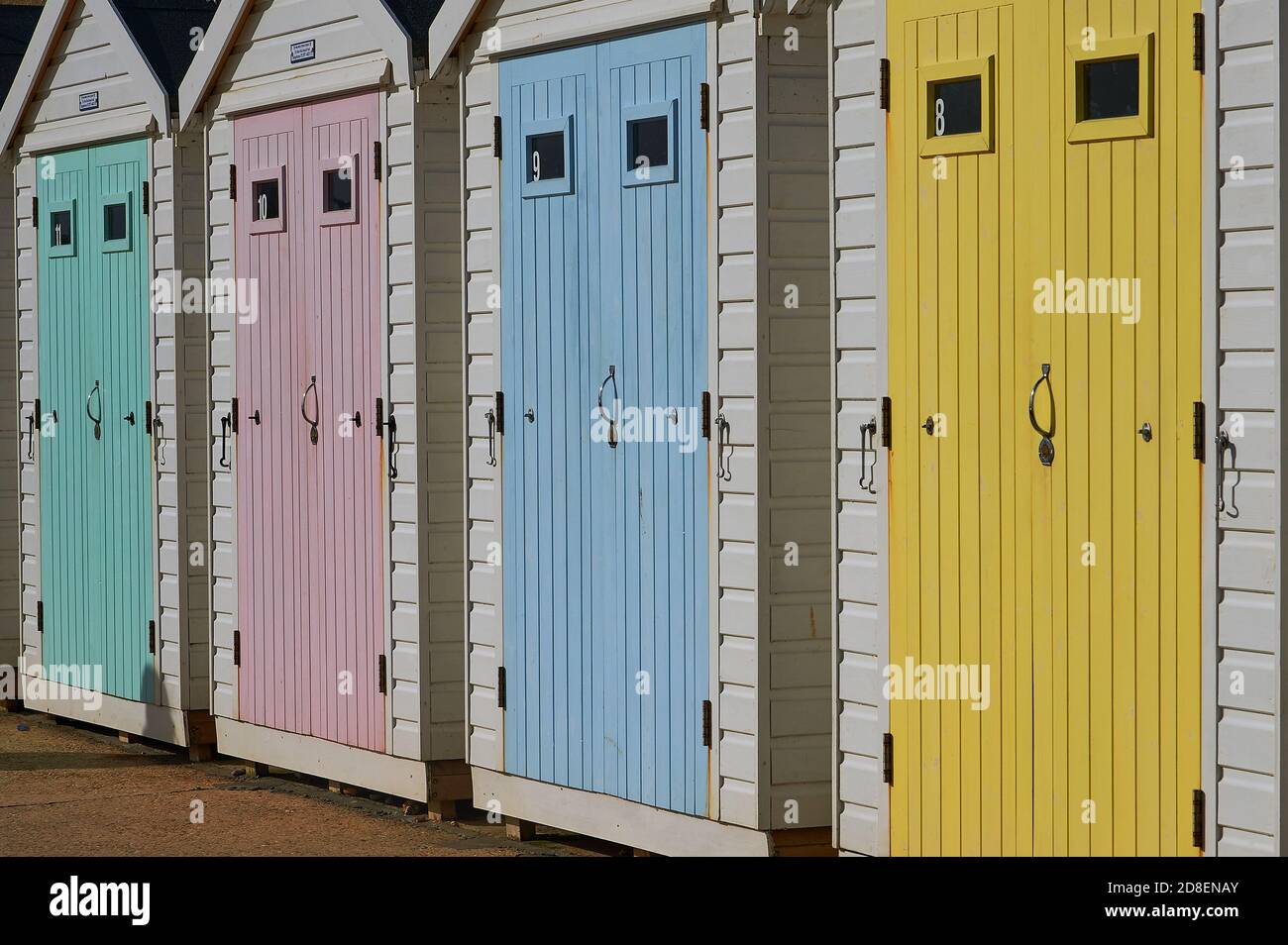 Lyme Regis, Dorset y puertas de madera de color pastel adornan cabañas de playa en el paseo marítimo. Foto de stock