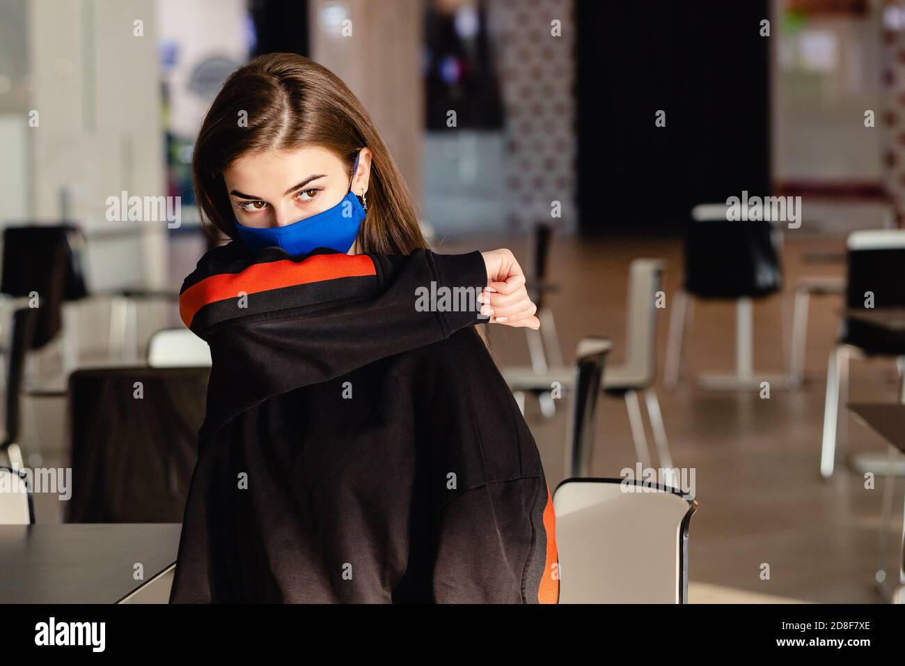 Retrato de una mujer joven con máscara protectora azul, estornudos y cubiertas con el codo. Protección y prevención de coronavirus. Foto de stock