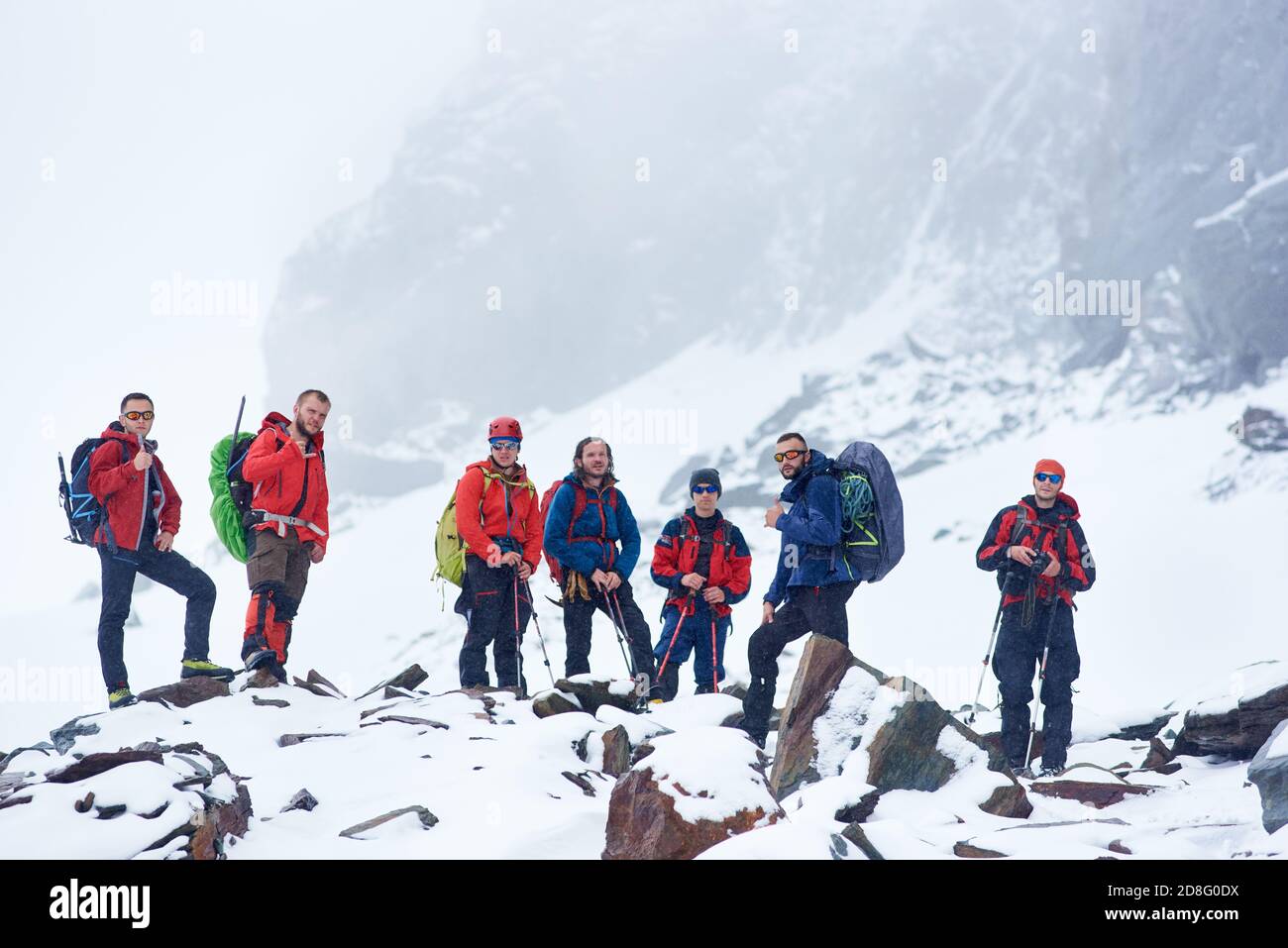 viajeros con mochilas y bastones de trekking tomando descanso durante la caminata en las montañas de invierno. Los excursionistas equipo de pie en rocas cubiertas de nieve. Conce Fotografía de