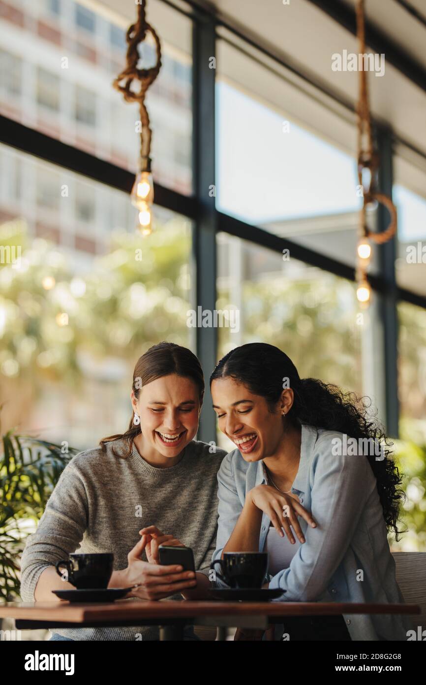 Dos mujeres sentadas en un restaurante mirando el teléfono móvil. Amigos sentados en un café con café en la mesa mirando el teléfono móvil. Foto de stock