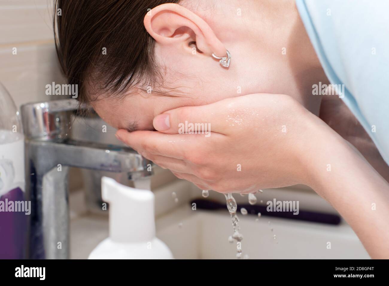 Lave la cara de una mujer con un chorro de agua, lave la cara en un fregadero bajo un chorro de agua fría. Cuidado facial de la piel en el hogar Foto de stock