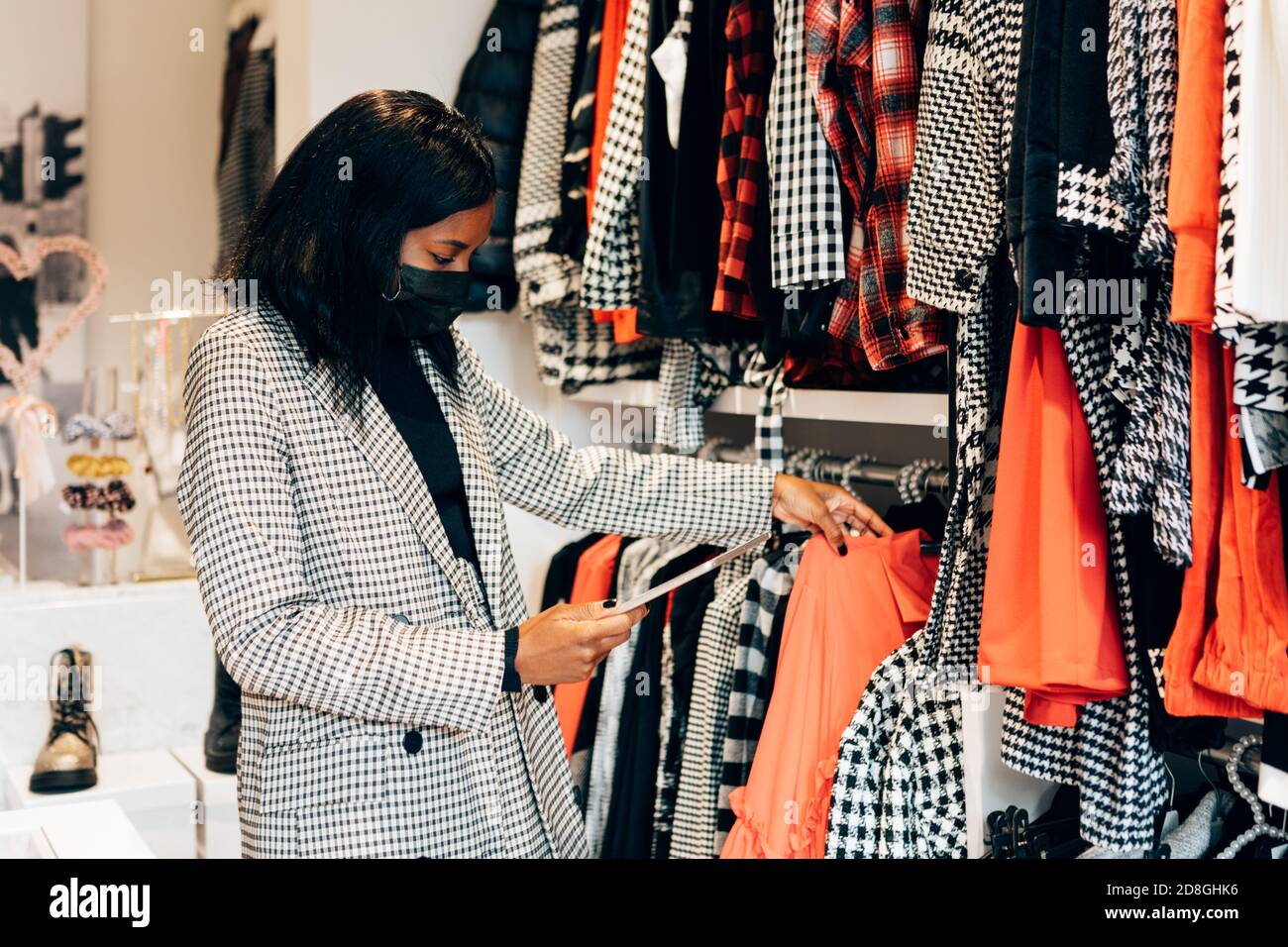 mujer negra gerente una tienda de moda está usando una máscara como protección contra el virus y el uso de una tableta para trabajar y el stock de la