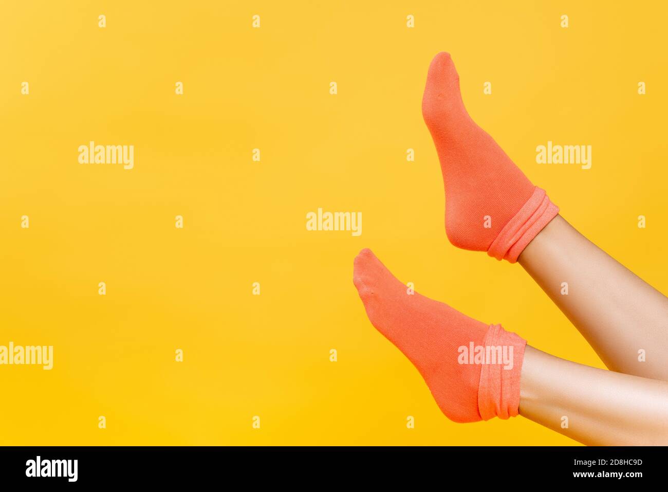 Vista recortada de las piernas femeninas en calcetines de color naranja suave aislados en amarillo Foto de stock