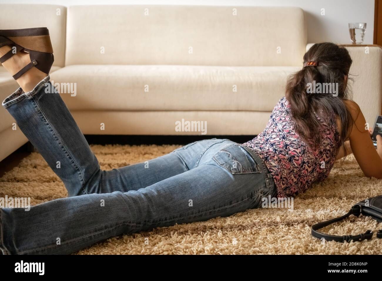 Mujer en pantalones vaqueros tumbados en la alfombra en la sala de estar y  tocando su teléfono móvil Fotografía de stock - Alamy