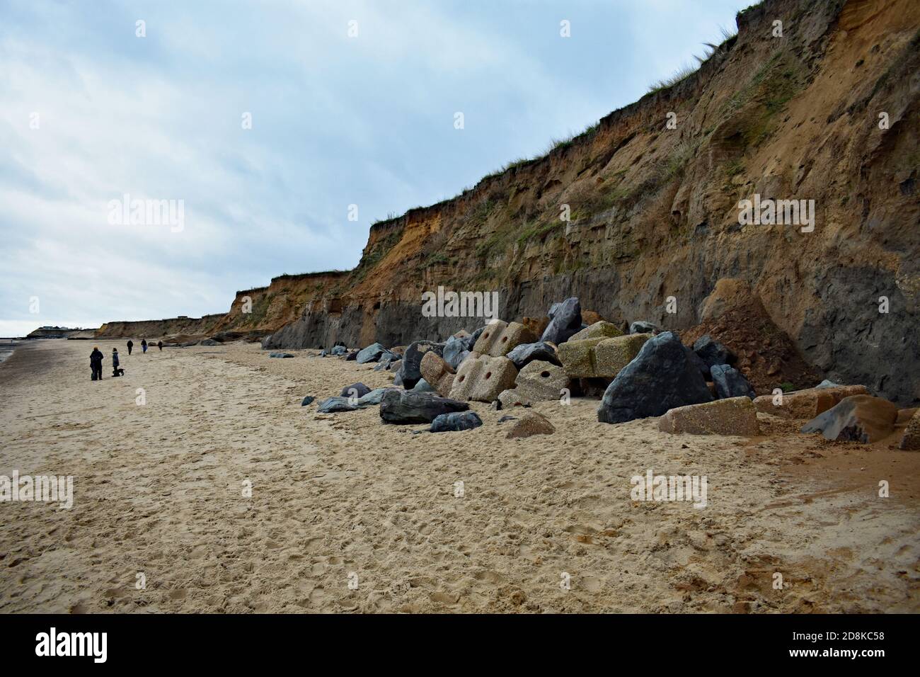 Los visitantes y los caminantes de perros caminan a lo largo de la base de los acantilados en la playa de Happisburgh, que están sometidos a la erosión costal en Norfolk, Inglaterra. Foto de stock