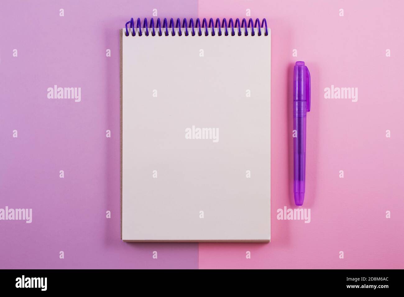 Un bloc de notas de color blanco con un espiral púrpura en un doble fondo violeta con un marcador de color púrpura junto a ella. Foto de stock