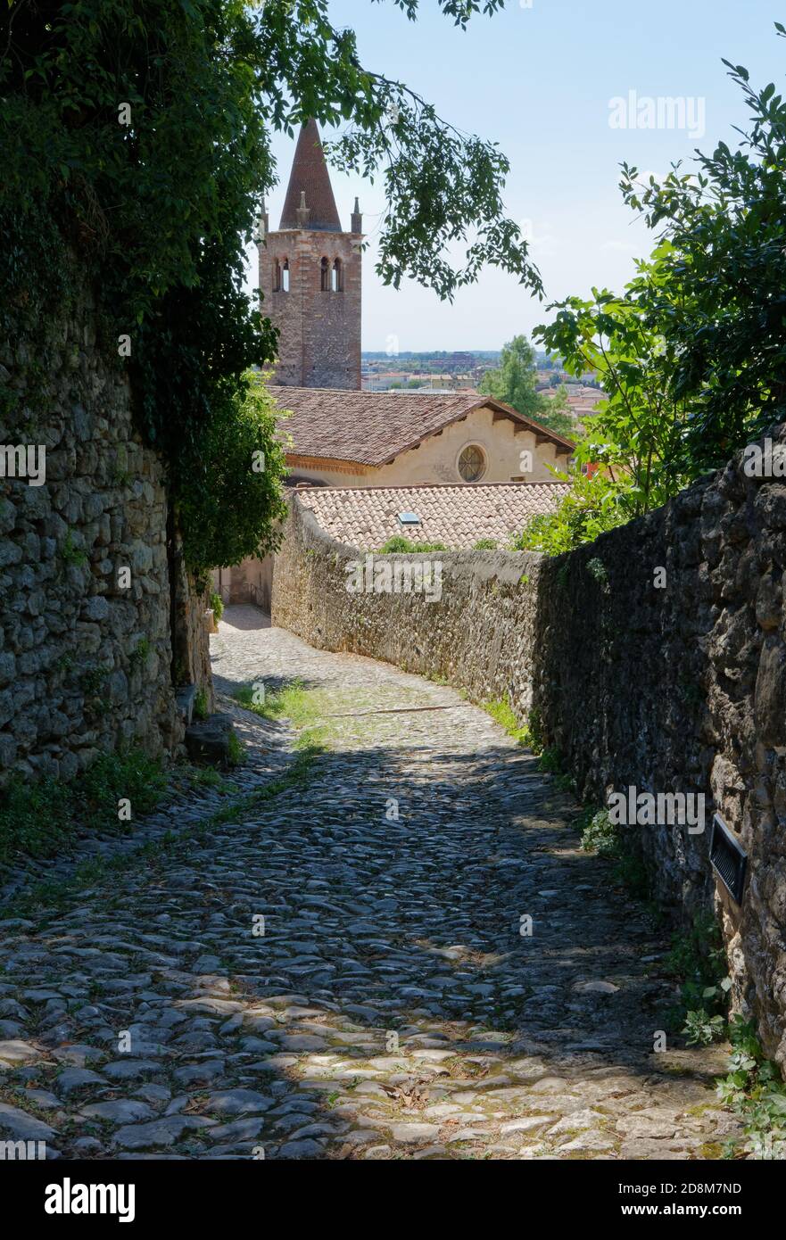 Sendero de adoquines que conduce desde el castillo hasta el centro de Soave, Italia, con la iglesia de Santa María de los padres dominicanos en el fondo Foto de stock