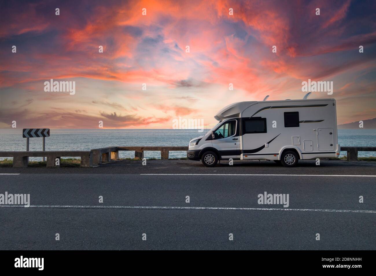 Caravana aparcada junto al mar al atardecer, con un cielo dramático Foto de stock