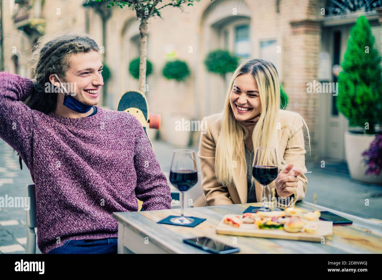 Pareja bebiendo vino tinto en el bar con máscaras de cara abierta En el tiempo de coronavirus - Nuevo concepto normal - enfoque en mujeres Foto de stock