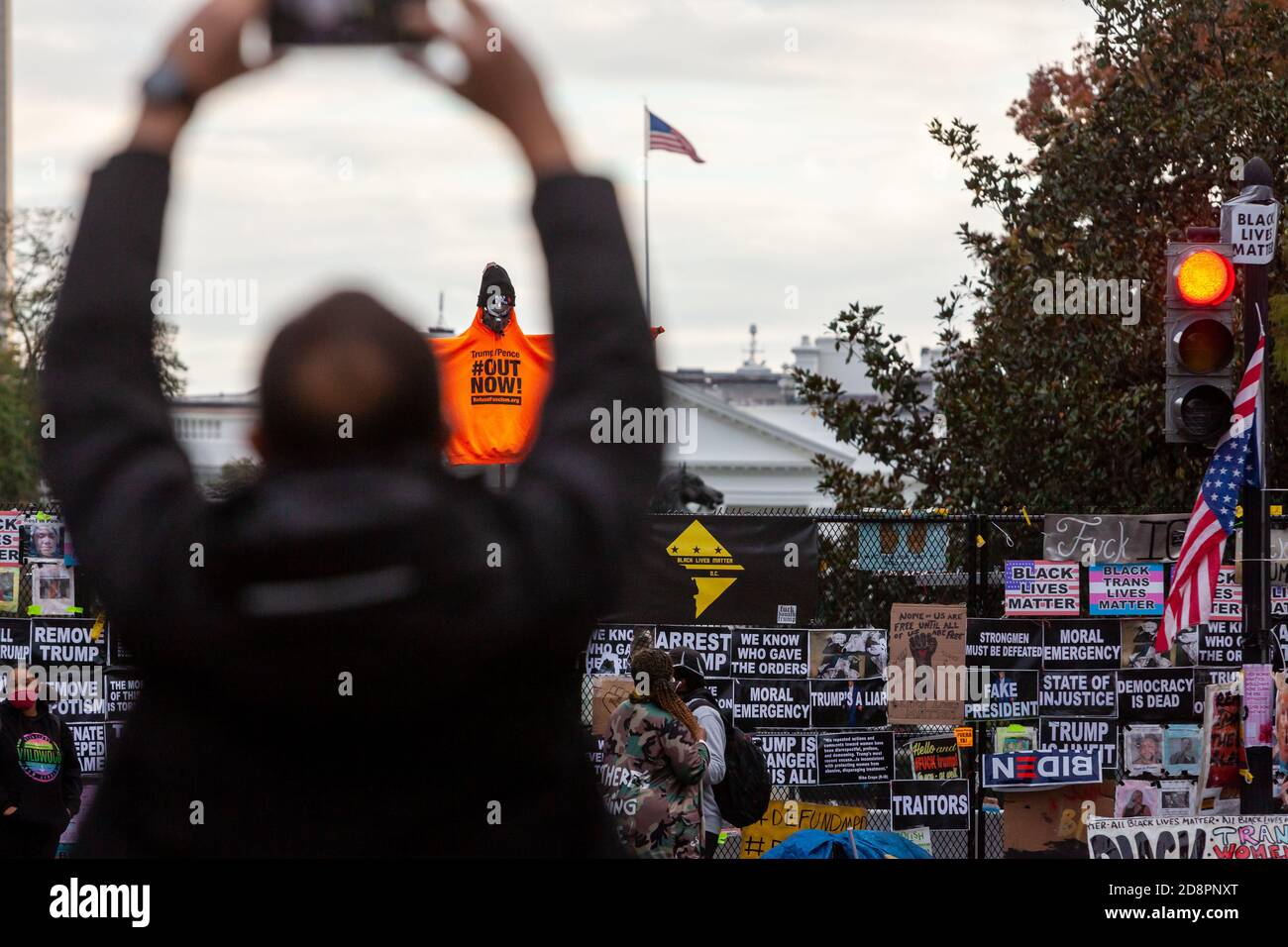 Washington, DC, EE.UU., 31 de octubre de 2020. Foto: Visitante de Black Lives Matter Plaza tomando una foto de una figura en un palo por encima de la valla de Lafayette Square en la Casa Blanca. La figura lleva la sudadera de color naranja del fascismo de la basura, y lleva el nombre de su iniciativa: ¡Trump/Pence Out Now! También lleva un sombrero Black Lives Matter. La Casa Blanca es visible detrás de la figura. Fotografiado durante una marcha llevada a cabo por Prefise Fascism DC para protestar contra las políticas fascistas y los abusos de la administración Trump. Crédito: Allison C Bailey/Alamy Live News Foto de stock