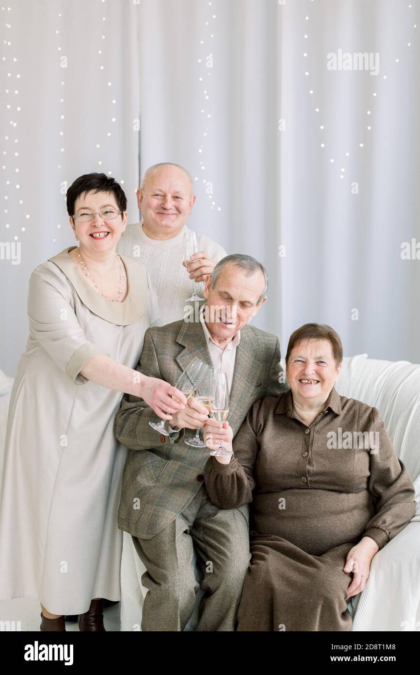 Feliz familia, pareja mayor, y pareja de edad, ropa elegante, posando para la foto en la época de Navidad, sosteniendo vasos con champán y Fotografía de stock -