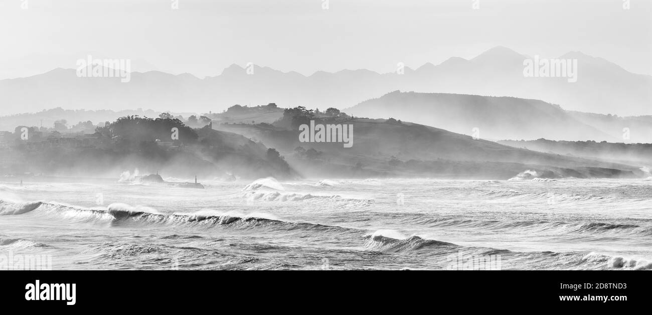 Un paisaje de montaña en silueta con playa y olas rompiendo en primer plano Foto de stock