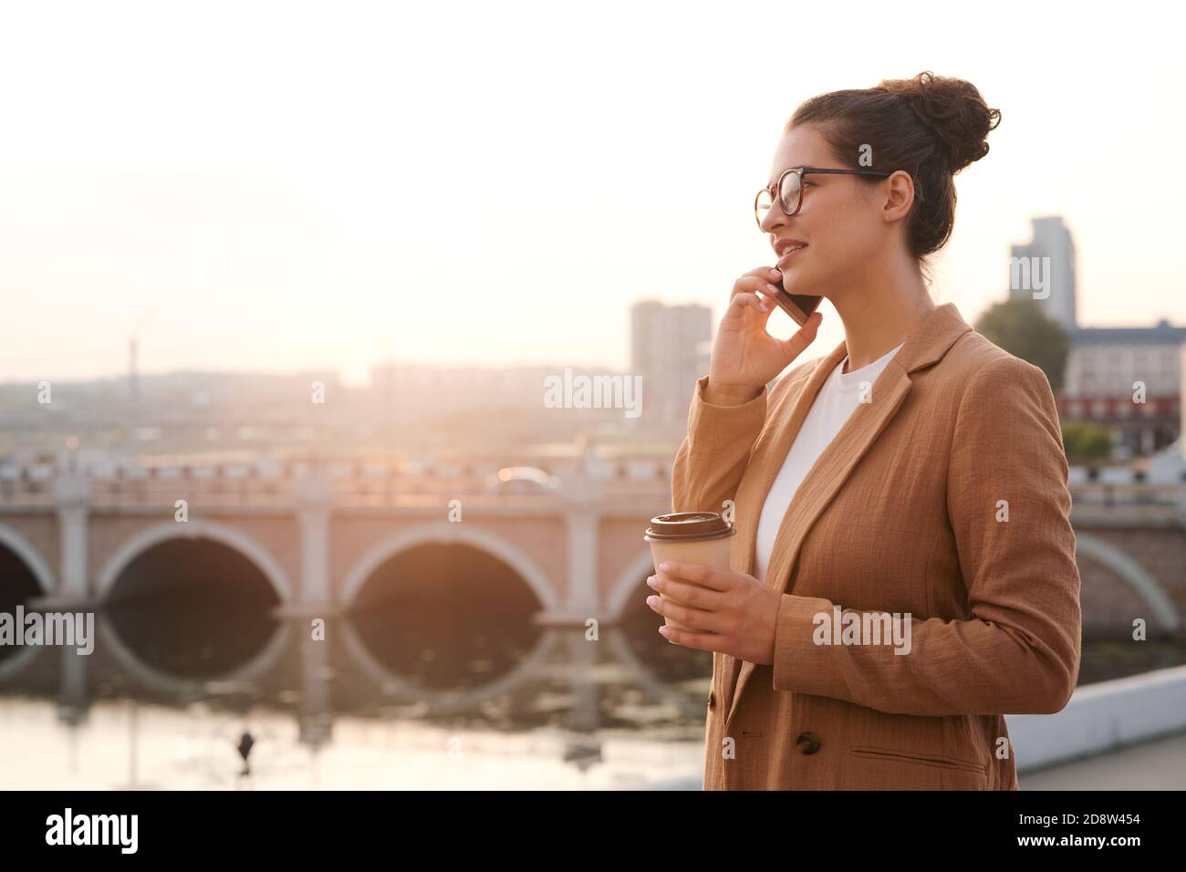 Mujer joven corredor o agente con vaso de café smartphone al oído Foto de stock