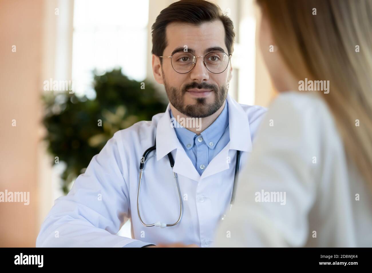 Amable y atento médico masculino escuchando las quejas de la paciente femenina Foto de stock