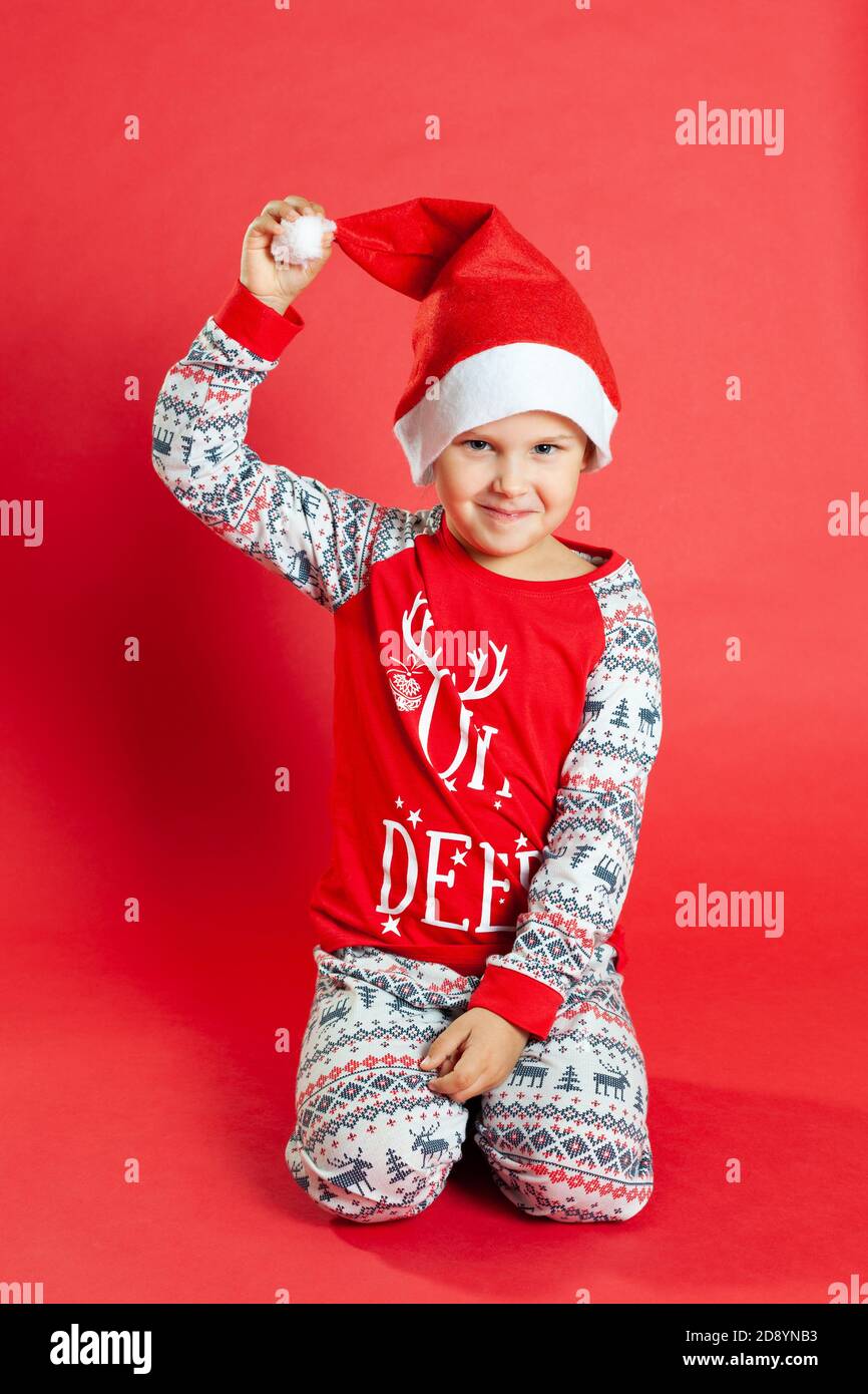 Niño sonriente de cerca en pijamas de Navidad se sienta en su regazo y se  sostiene con el sombrero de Santa Claus, aislado sobre fondo rojo  Fotografía de stock - Alamy