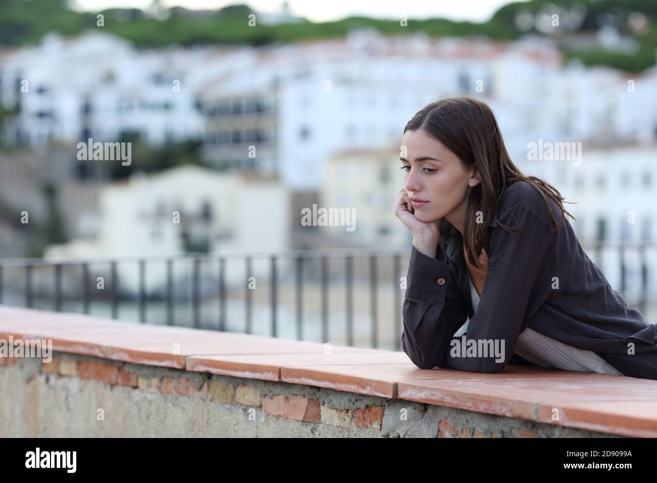 Triste mujer quejándose solo mirando hacia abajo en un balcón adentro una ciudad en la playa Foto de stock